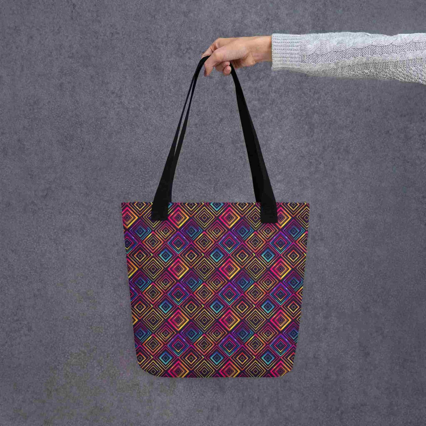 A 15x15 inch tote bag with black handles, which features a neon tapestry design in a sophisticated blend of colors, held by a lady's hand. Grey background.