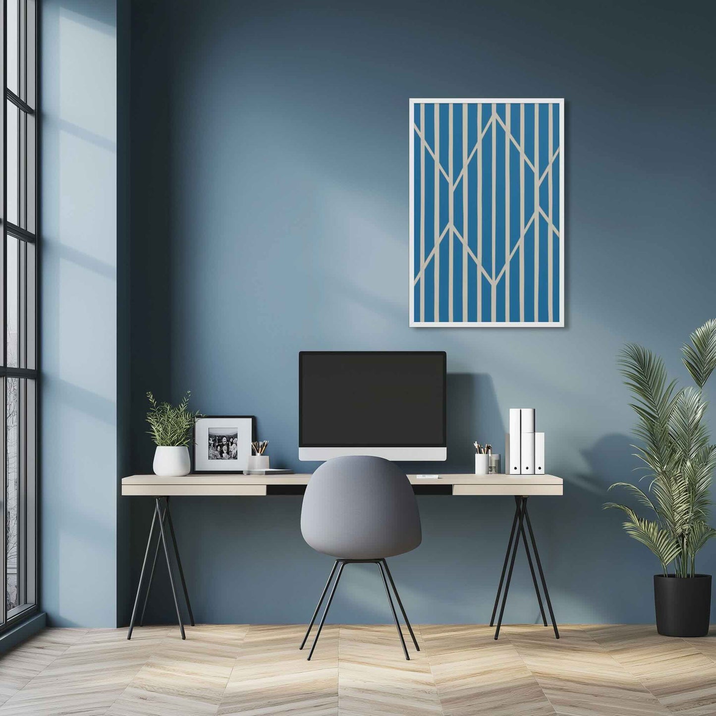 Illustration 2 of a compelling piece of blue and white abstract art, OBLIQUE, in framed poster. This sophisticated design creates visual drama as static vertical stripes are dynamically intersected by bold, angular white lines. The result is a striking, kinetic composition perfect for modern interiors. The framed poster hangs over a desk in a study room.