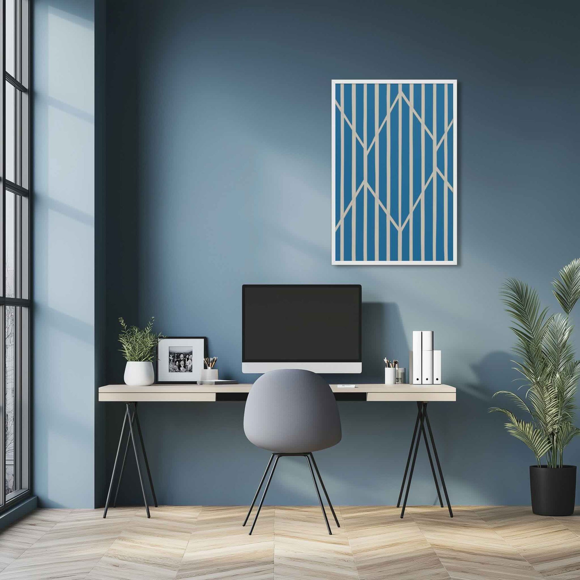 Illustration 2 of a compelling piece of blue and white abstract art, OBLIQUE, in framed poster. This sophisticated design creates visual drama as static vertical stripes are dynamically intersected by bold, angular white lines. The result is a striking, kinetic composition perfect for modern interiors. The framed poster hangs over a desk in a study room.