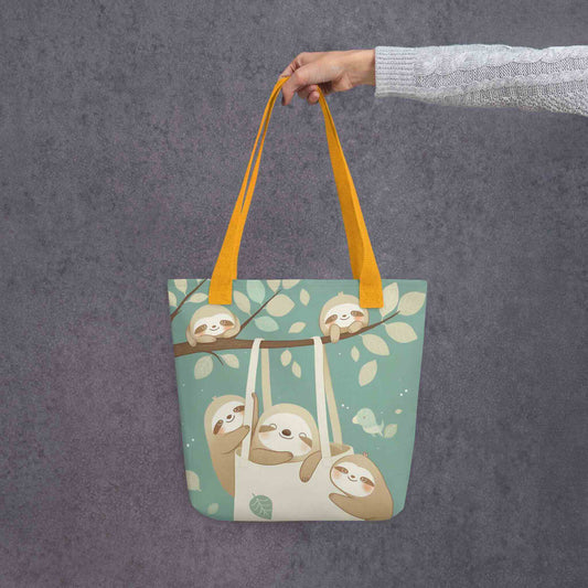 The cutest sloth tote bag you'll ever carry! This charming, sophisticated design captures the tranquility of the forest, with yellow shoulder handles, held in a hand. Grey background.
