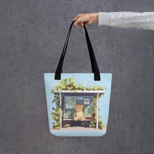 Teddy Bear Tote Bag which features a cute teddy bear waiting sweetly at the bus-stop, in a charming, tranquil setting in nature, with green and mint tulip colors. Black handles. Dimension 15x15 inch polyester. Grey background.