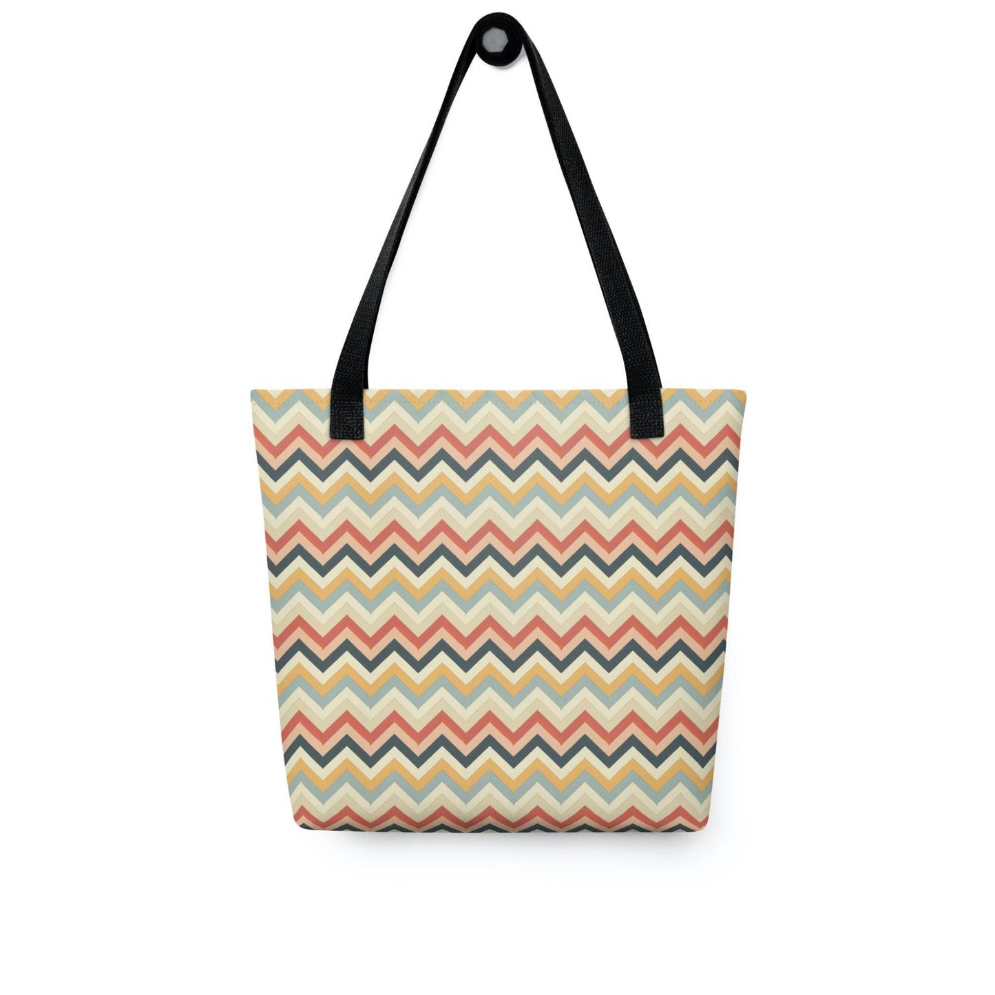 A 15x15 inch tote bag with black handles, in a multicoloured pattern of Zig Zag lines, hanging on a wall. White background.