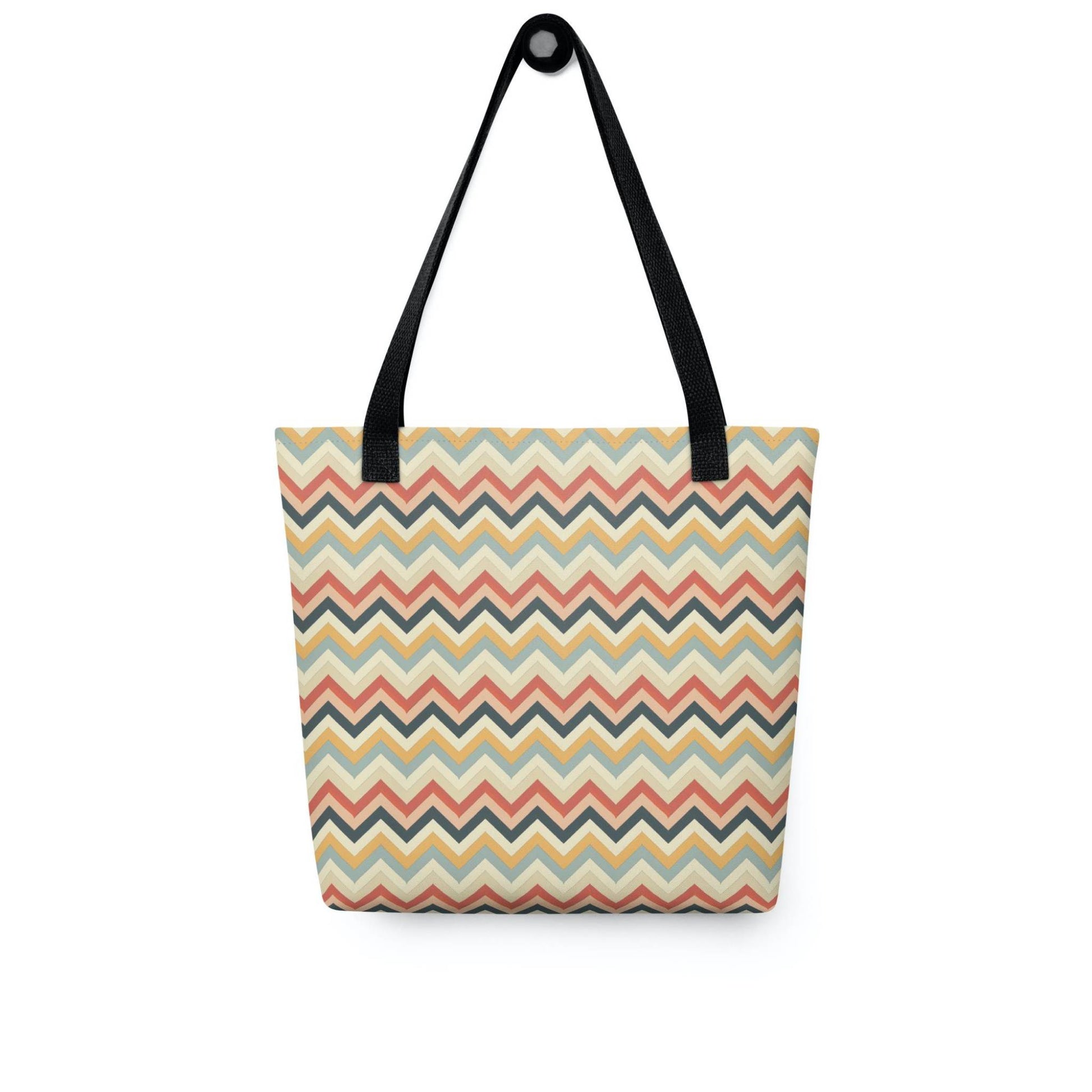 Zig zag tote bag with black handles, in a multicoloured pattern of Zig Zag lines, hanging on a white wall. Dimension 15x15 inches. White background.