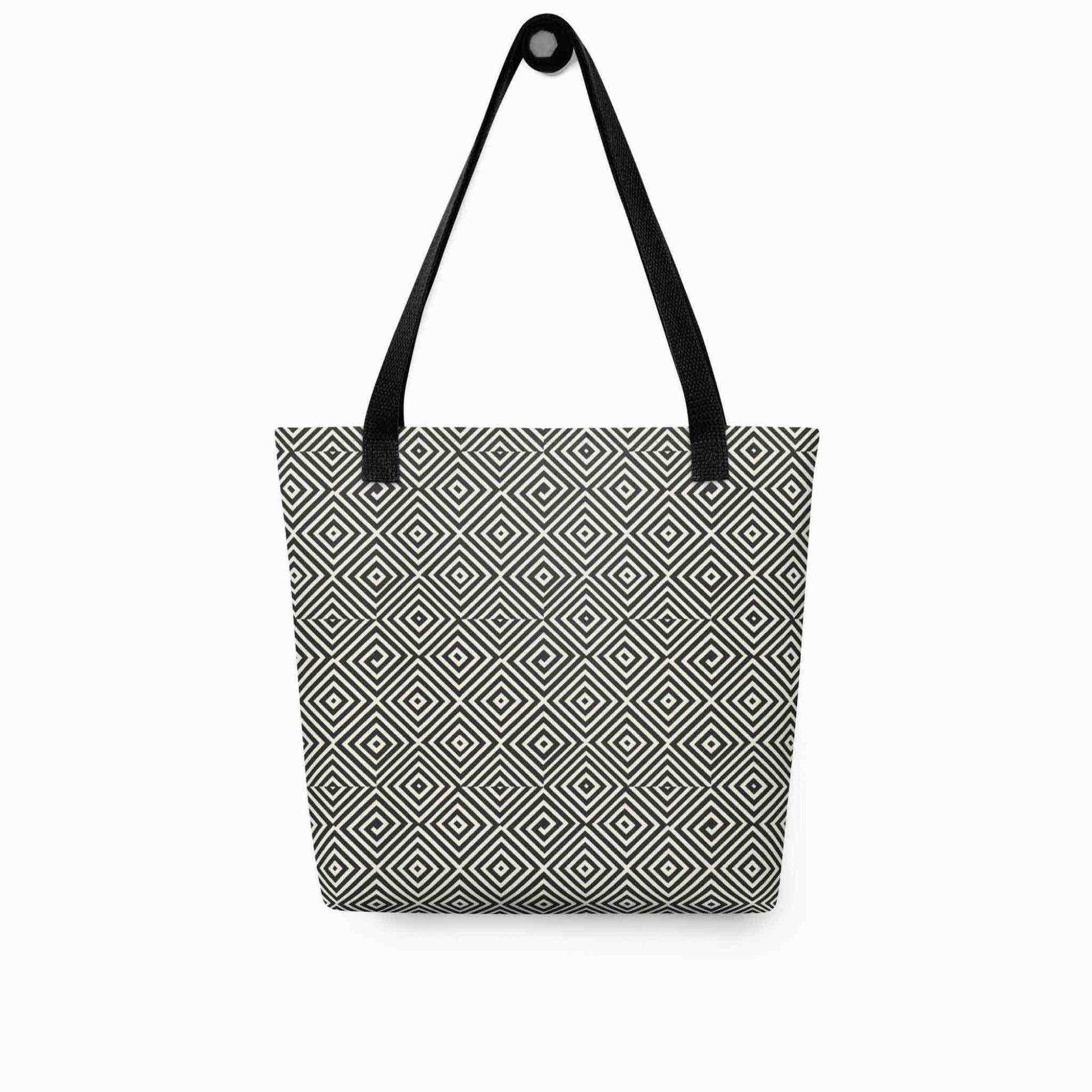 A diamond pattern tote bag with black handles, which features a mesmerizing black and white geometric look, hanging on a white wall.