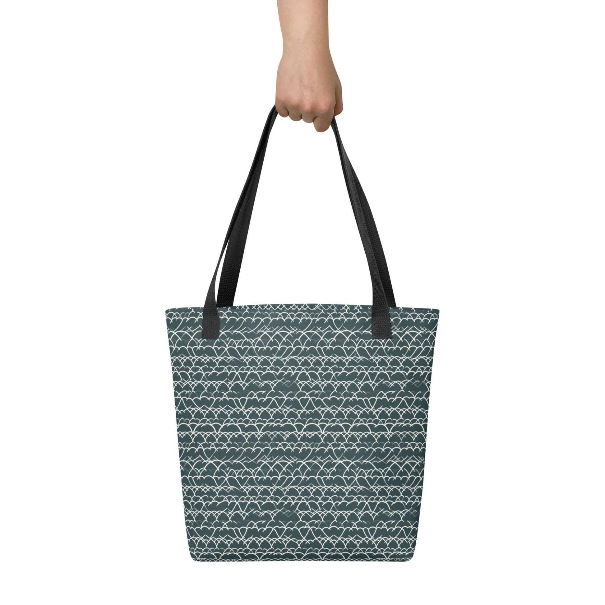 A 15x15 inch tote bag with black handles, which features white geometric lace design that dances across a refreshing blue background, held by a hand. White background.