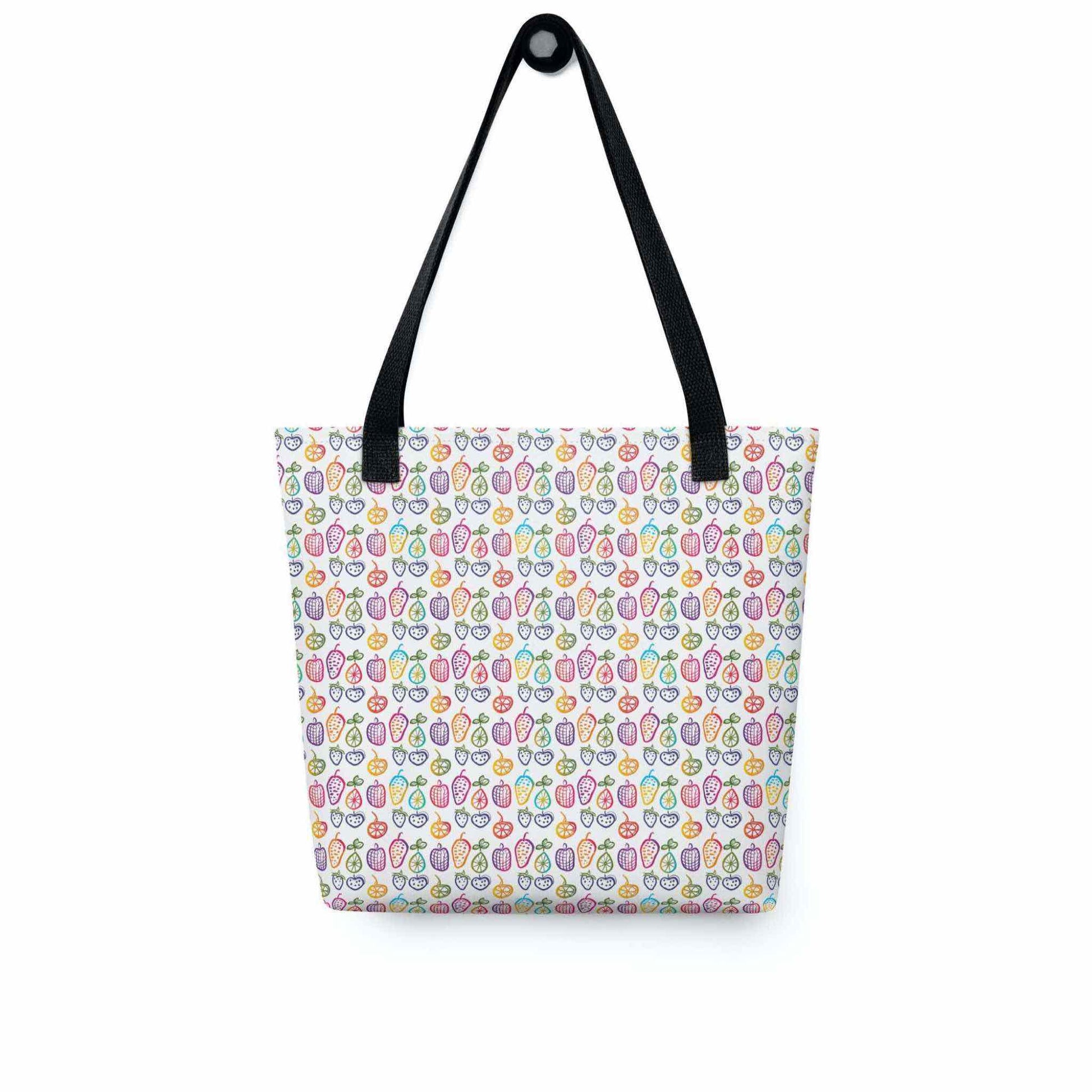 A 15x15 inch tote bag with black handles, which features colourful cheerful doodles of fruits in a crisp white background, hanging on a wall hook. White background.