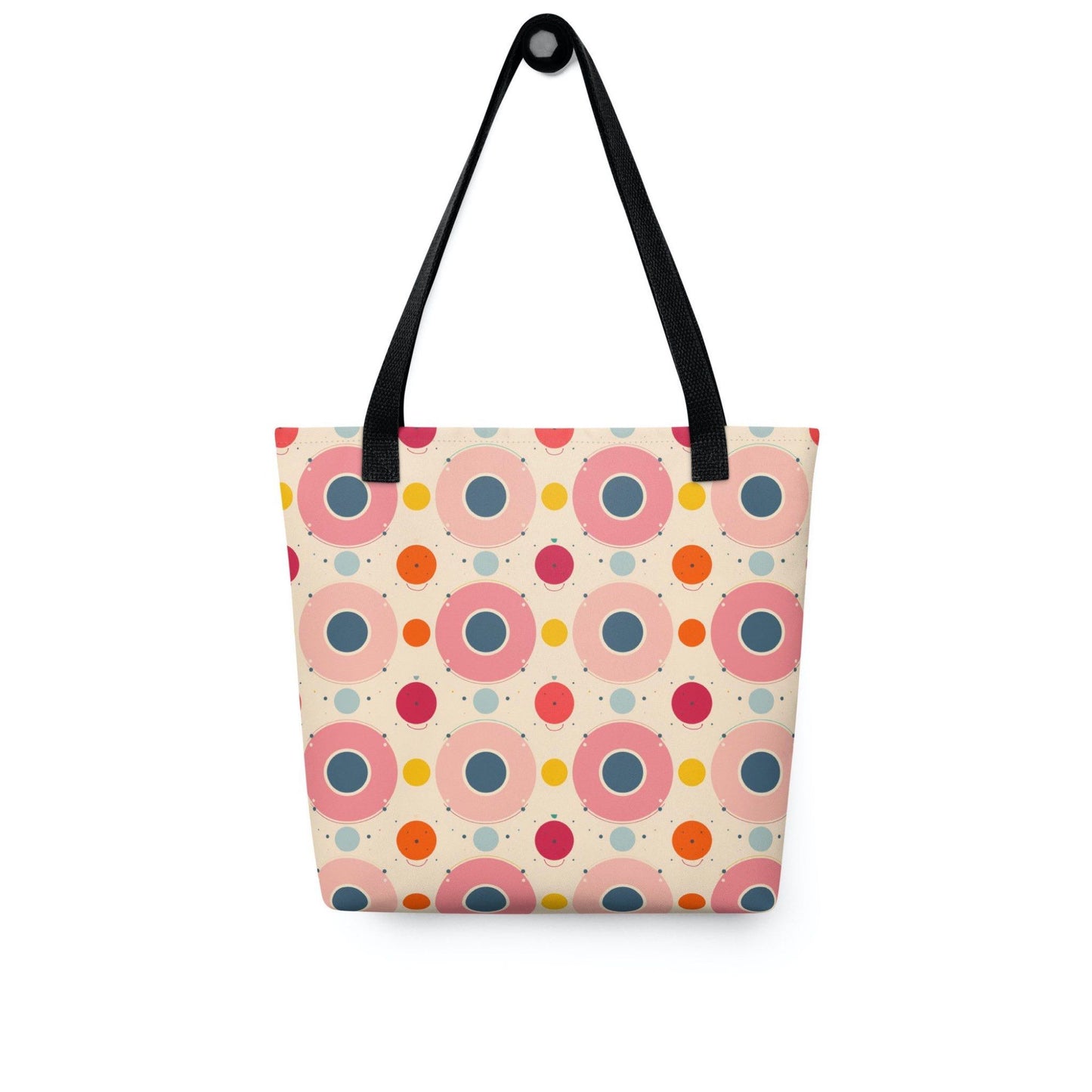 A 15x15 inch tote bag with black handles, which features an artsy design of pastel candy pops of colors in a beige background, hanging on a wall hook. White background.