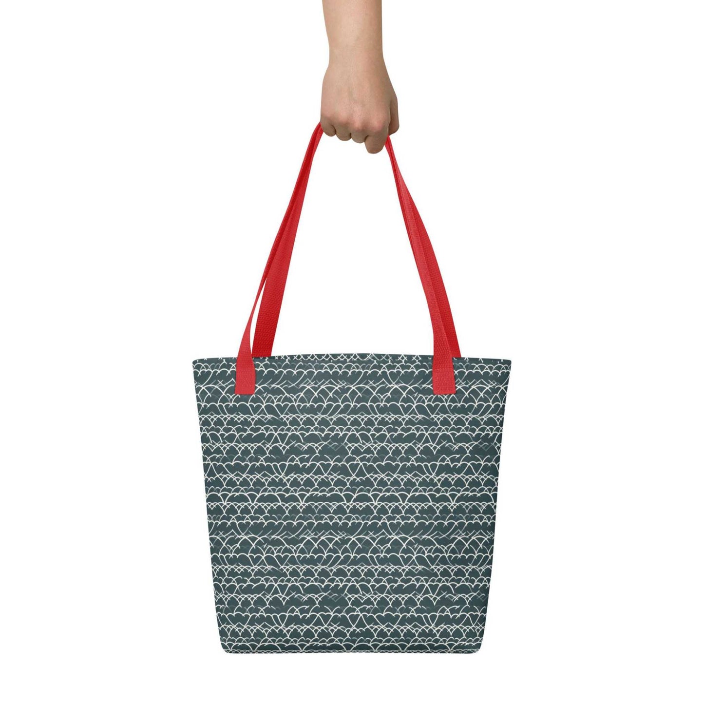 A 15x15 inch tote bag with red handles, which features white geometric lace design that dances across a refreshing blue background, held by a hand. White background.