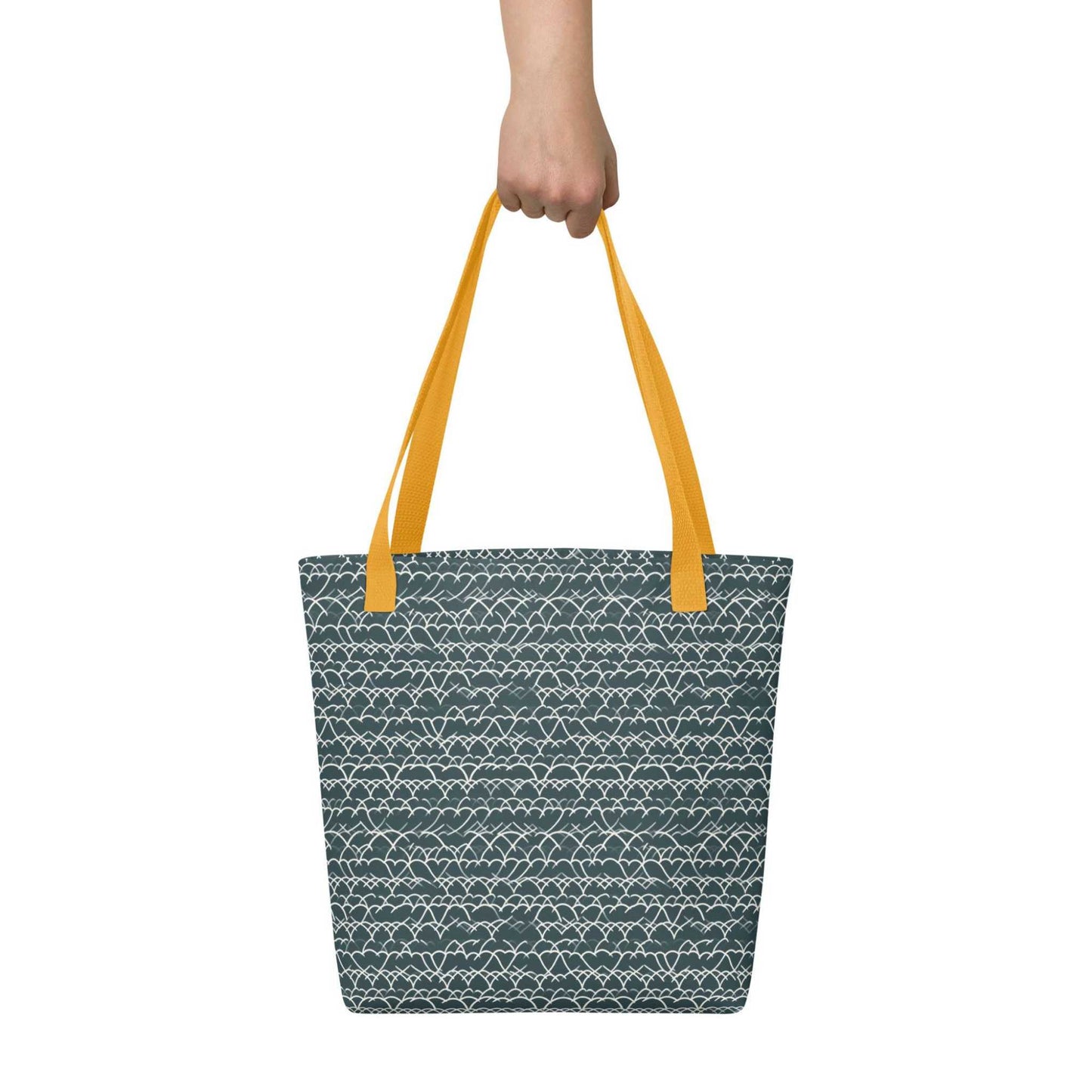 A 15x15 inch tote bag with yellow handles, which features white geometric lace design that dances across a refreshing blue background, held by a hand. White background.